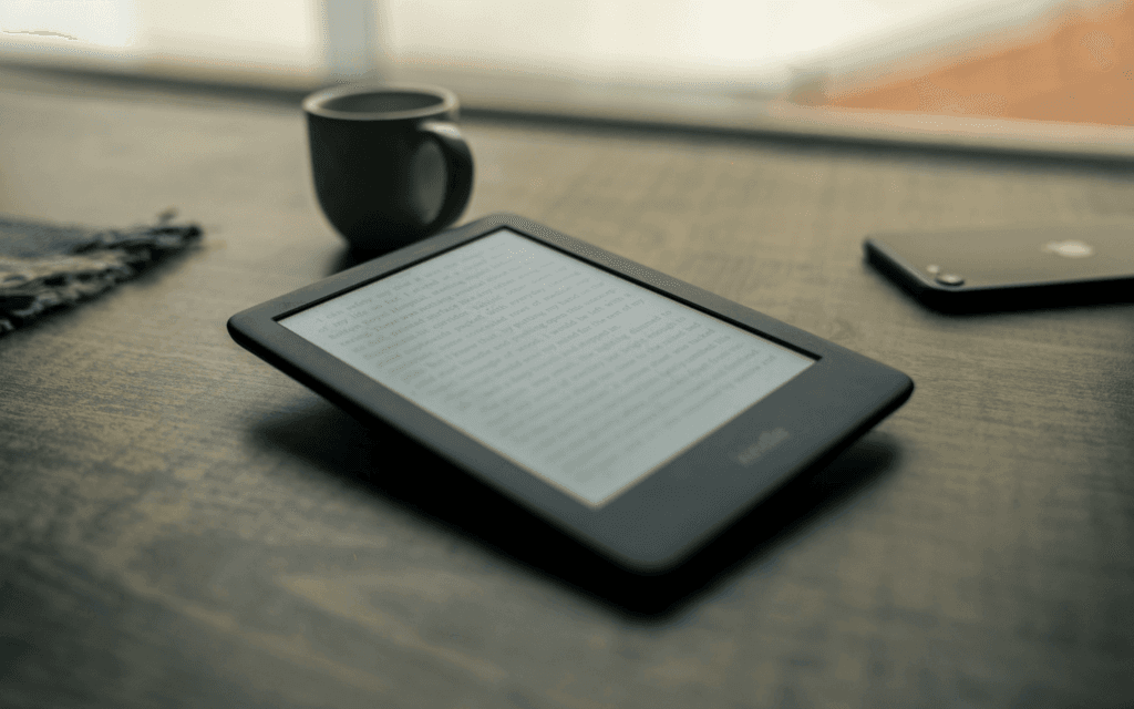 An e-reader displaying a page possibly about lead magnets, on a wooden surface beside a cup of coffee and a smartphone, representing a serene reading setup.