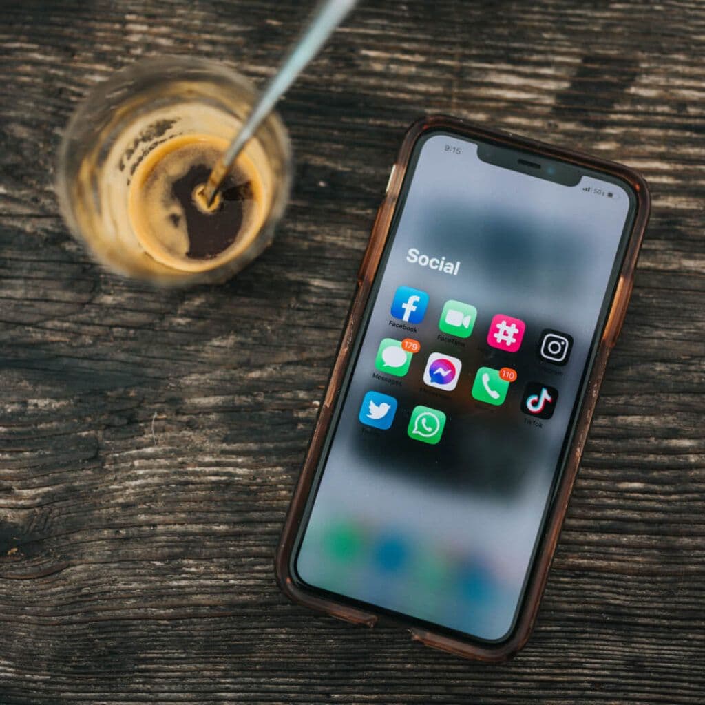 Smartphone with social media apps on screen, lying next to a coffee cup stain on a wooden surface, representing the tools for creating a social media analytics report PDF