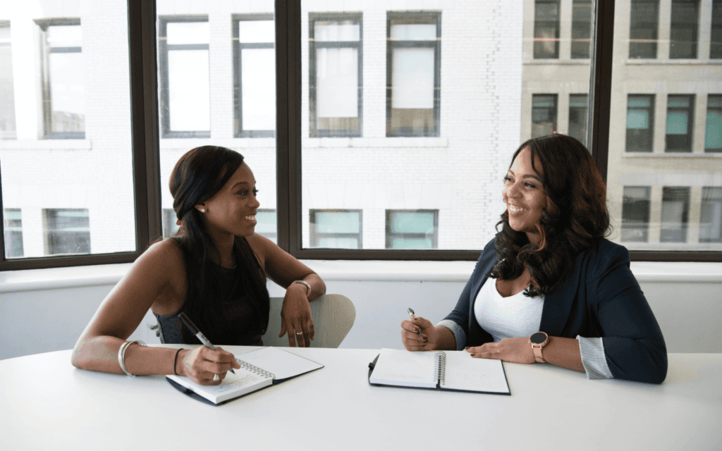 Two consultants in a discussion at an office, possibly reviewing the 'Best CRM for Digital Marketing Agency', underscored by the ambient light and urban view from the office windows.