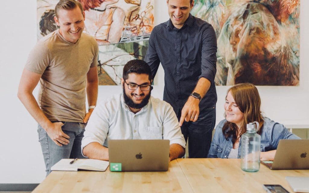 A team of professionals engaging in a collaborative discussion over a laptop, likely analyzing data with KPI reporting tools.