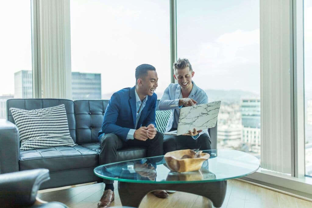Two men sitting on a sofa, reviewing content on a laptop, representing the use of AI tools for marketing to analyze data and optimize strategies.