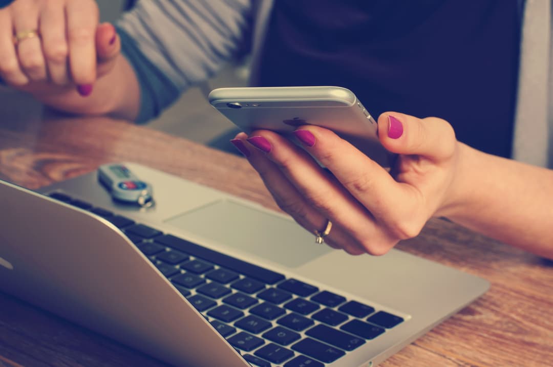 An image of a macbook and a women holding a phone.