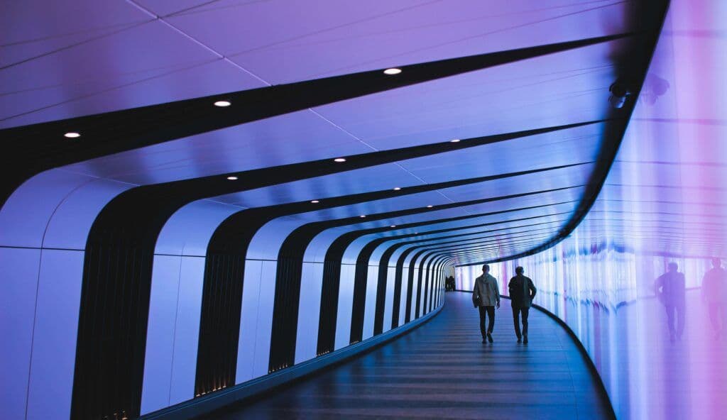 Two people walking through a futuristic, brightly lit hallway, symbolizing the innovative role of AI tools in advancing marketing strategies.