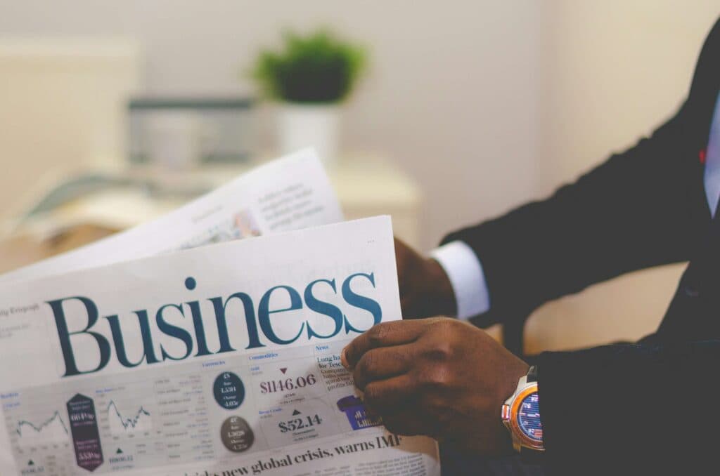 Person reading a business newspaper with financial data, symbolizing the use of AI tools for marketing to stay updated on market trends.