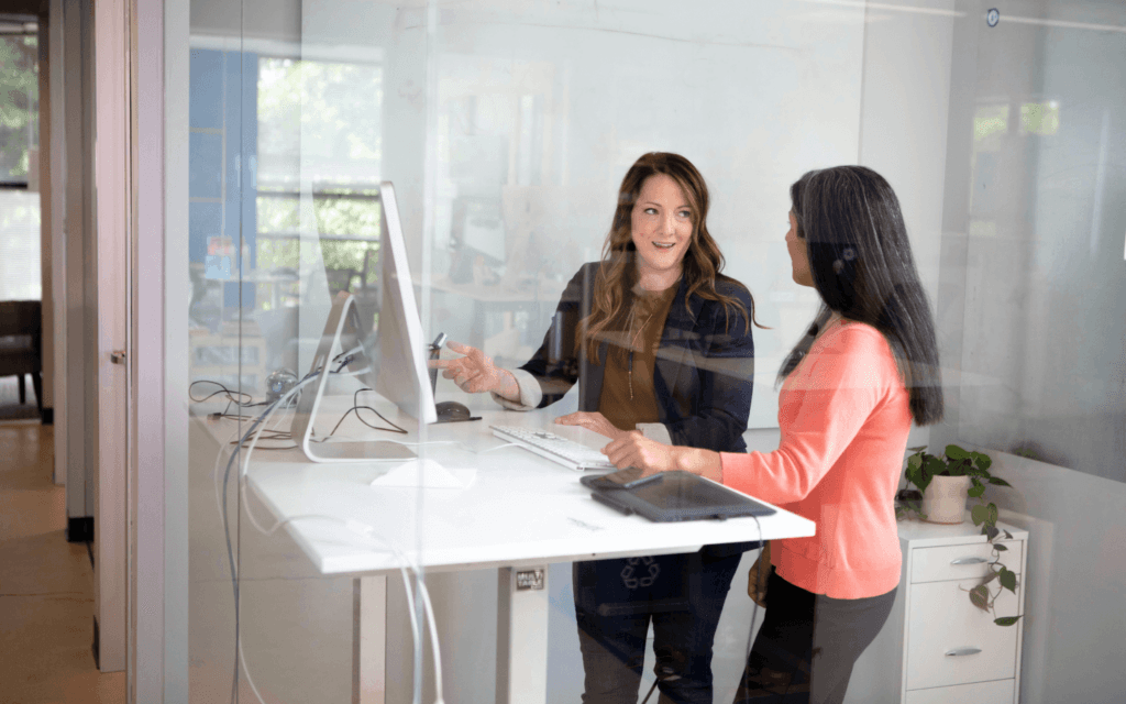 Two businesswomen discussing an 'Ideal Customer Profile' at a computer workstation in a modern office setting.