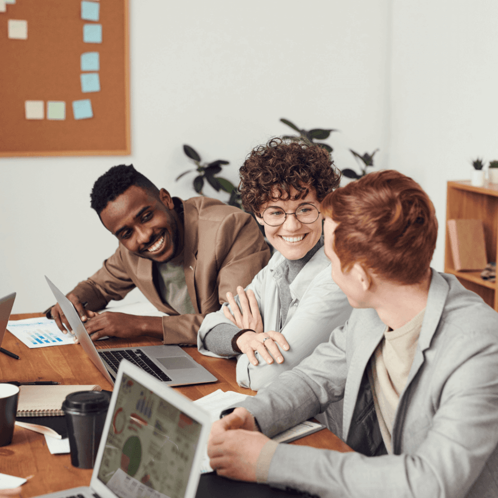 A cheerful team of professionals in a casual meeting, possibly reviewing data from the Best SEO Report Software on their laptops, in a bright and modern office.