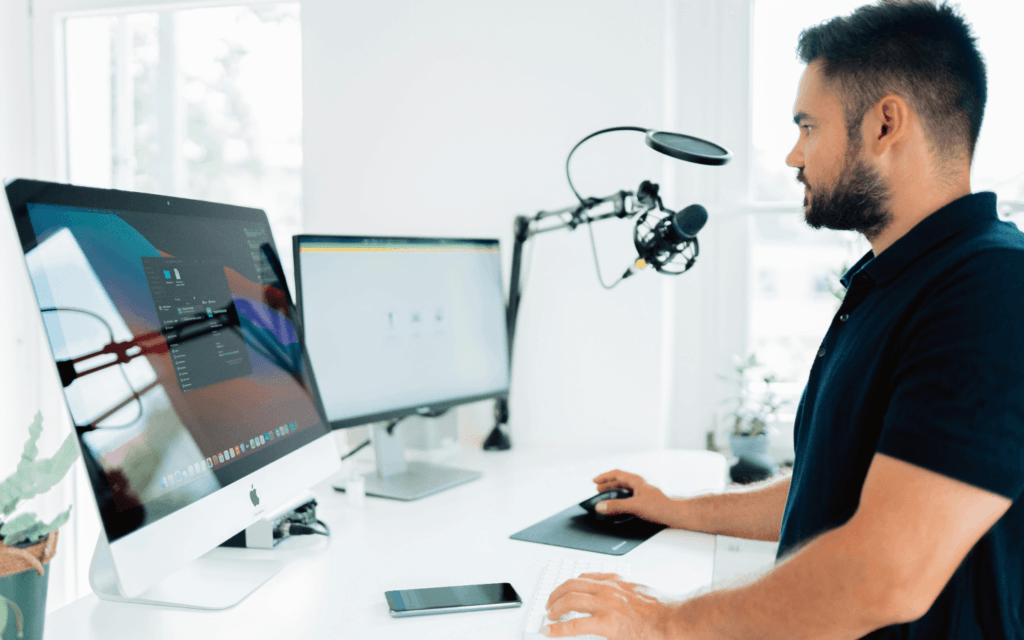 digital marketer focused on an influencer marketing project using a desktop computer and graphics tablet in a well-lit office, with a podcasting microphone setup in the background.