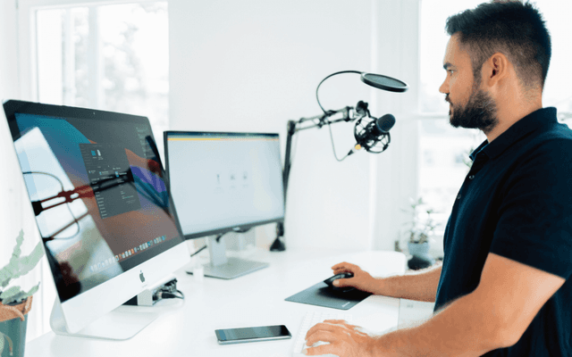 digital marketer focused on an influencer marketing project using a desktop computer and graphics tablet in a well-lit office, with a podcasting microphone setup in the background.