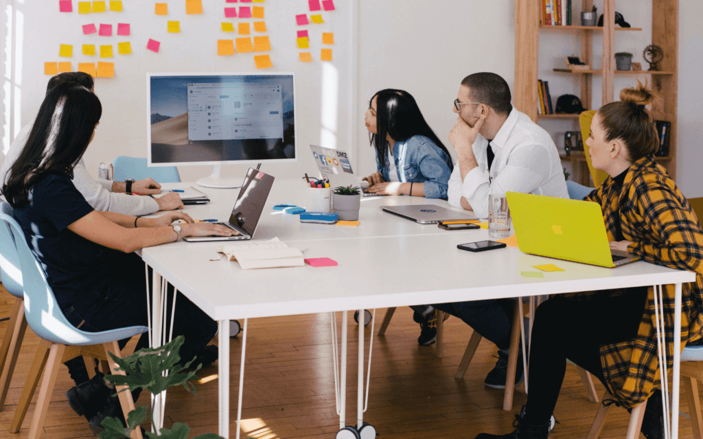 A team of professionals collaborating around a table with laptops, discussing digital marketing innovations in a modern workspace.