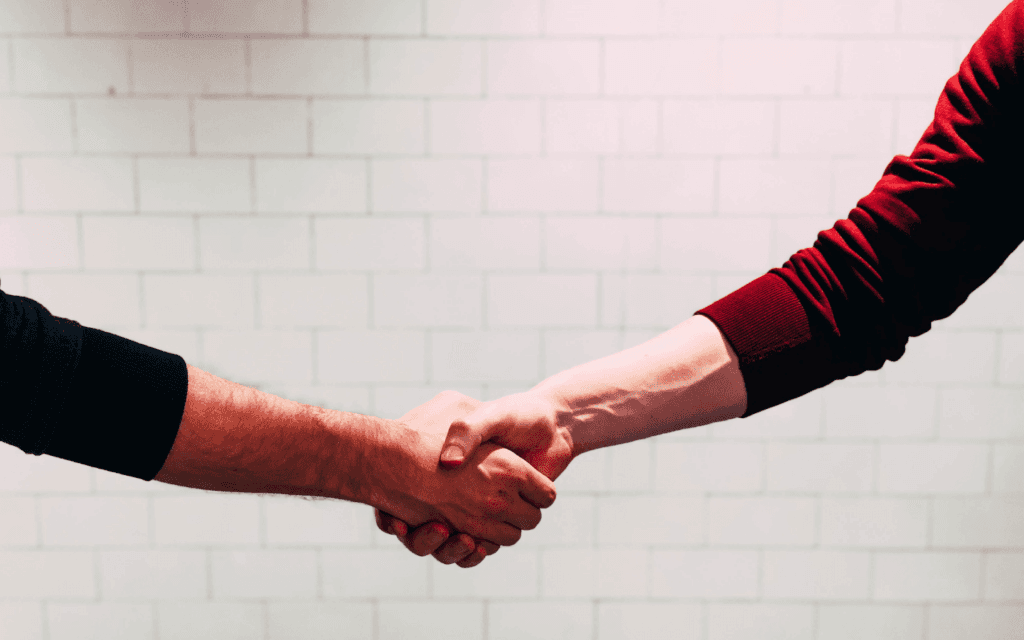Two individuals engaging in a handshake, representing the collaborative spirit and partnership agreements within a Digital Agency Workflow, set against a white brick wall for a professional look.