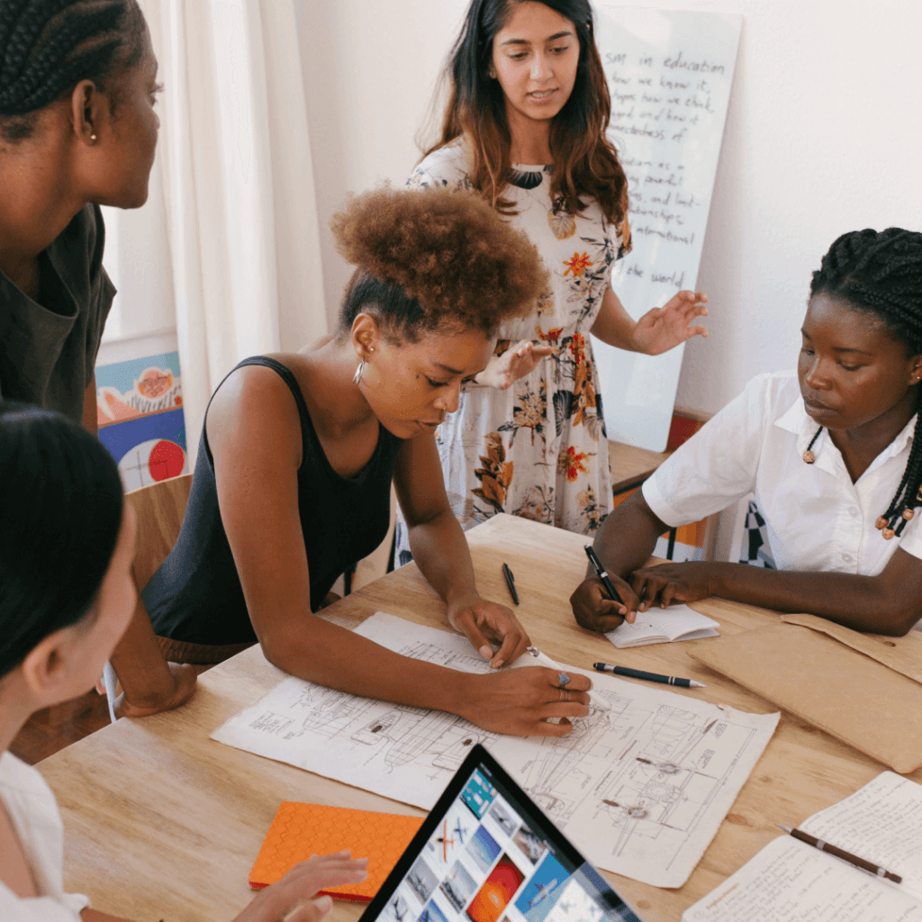 "Diverse group of women analyzing data during a team meeting, possibly reviewing an Instagram Insights Report on a tablet for social media strategy development."