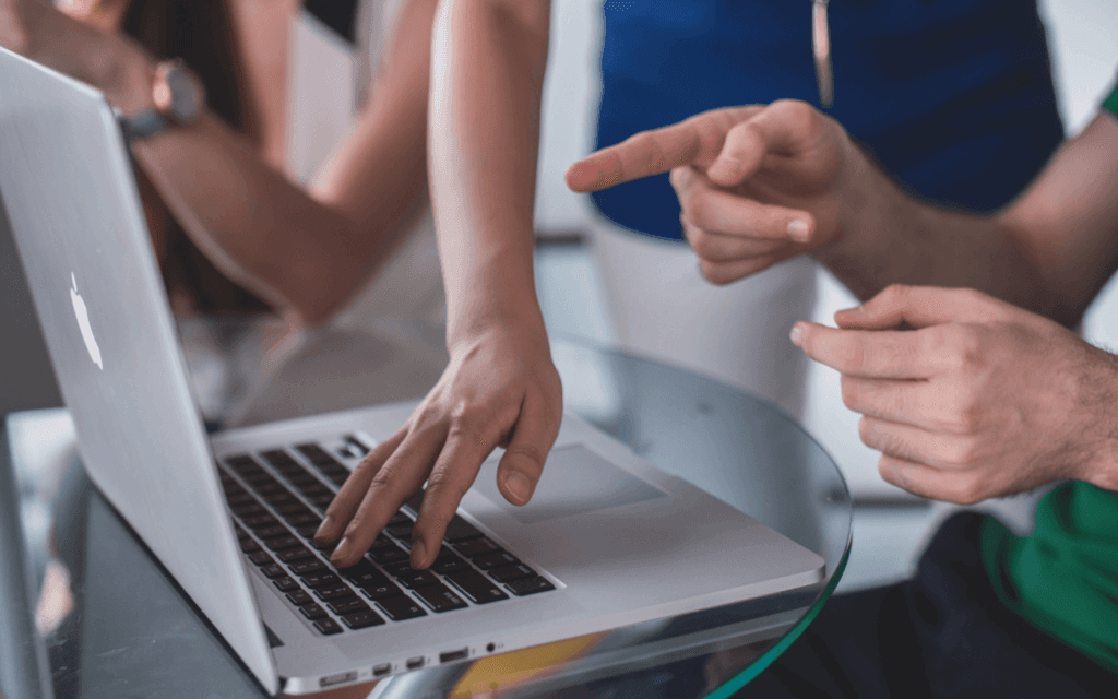Two individuals collaborating on a laptop, using custom reporting tools to analyze and discuss data reports, with a focus on one's hands typing and the other's pointing.
