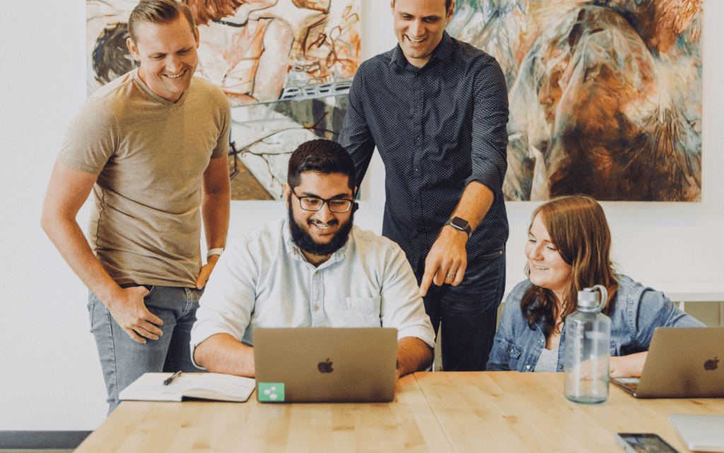 A motivated team of professionals collaboratively discussing the 'Best CRM for Digital Marketing Agency', around a laptop in a modern office setting