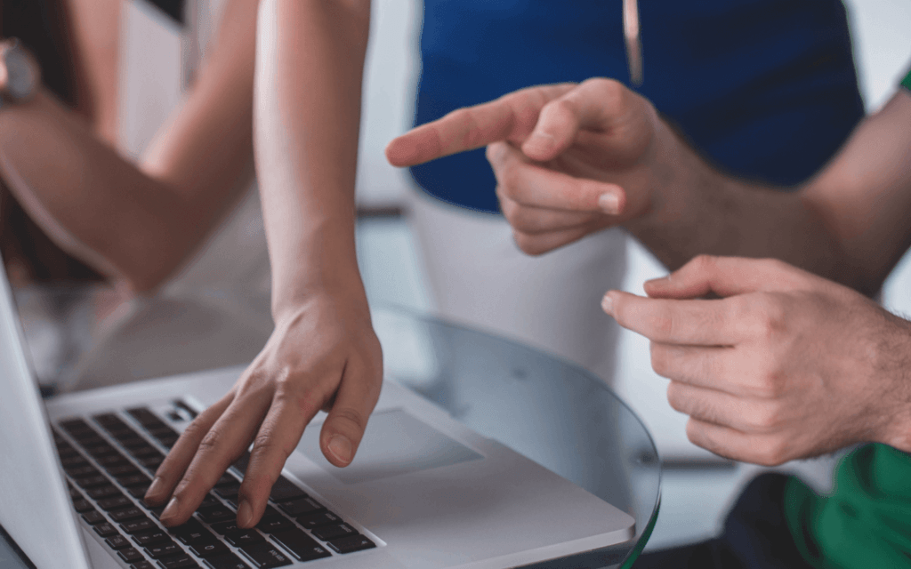 Two marketing professionals discussing an email campaign report on a laptop in an office setting, one pointing at the screen and the other typing, indicating an interactive evaluation of campaign performance.
