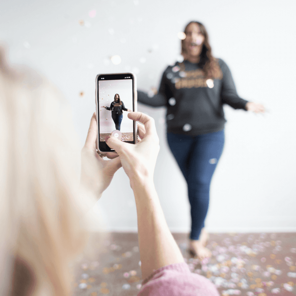 A smartphone capturing a woman's photo amid falling confetti, showcasing the vibrancy of digital marketing innovations in content creation.
