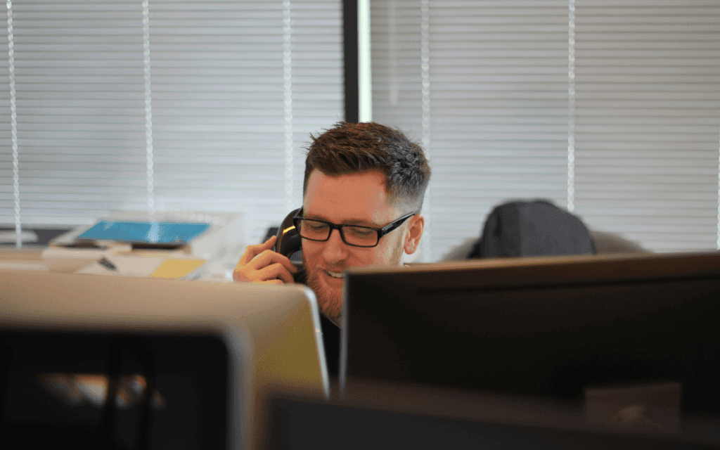 Smiling business professional in an office on a phone call, embodying effective client retention communication.