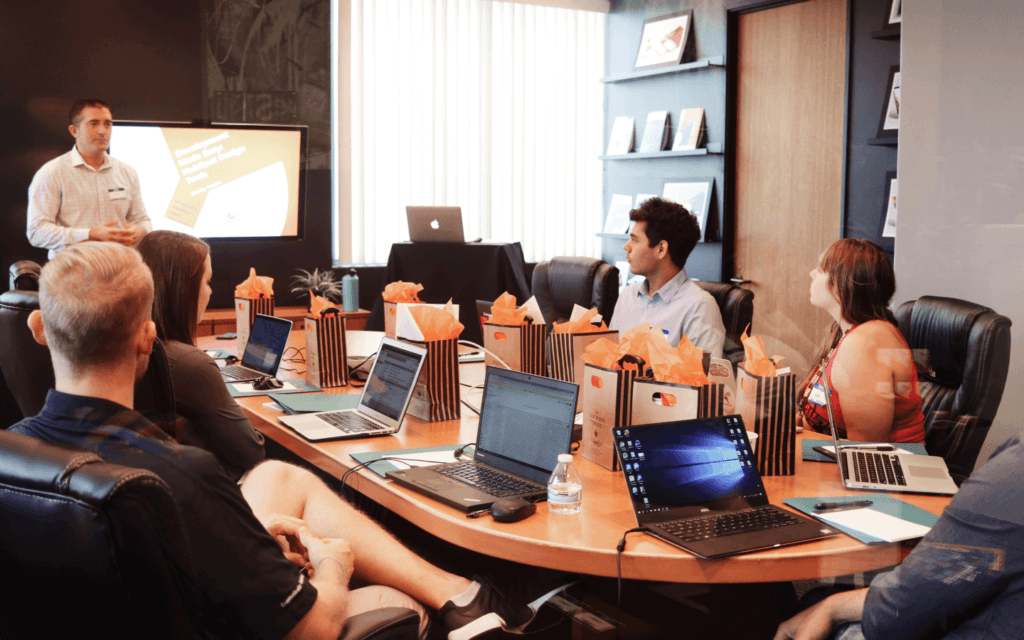 A professional team attends a presentation on 'Blended Query Builder, Enhanced Features & New Data Sources' in a corporate setting, reflecting active participation and focus on advanced data management techniques.