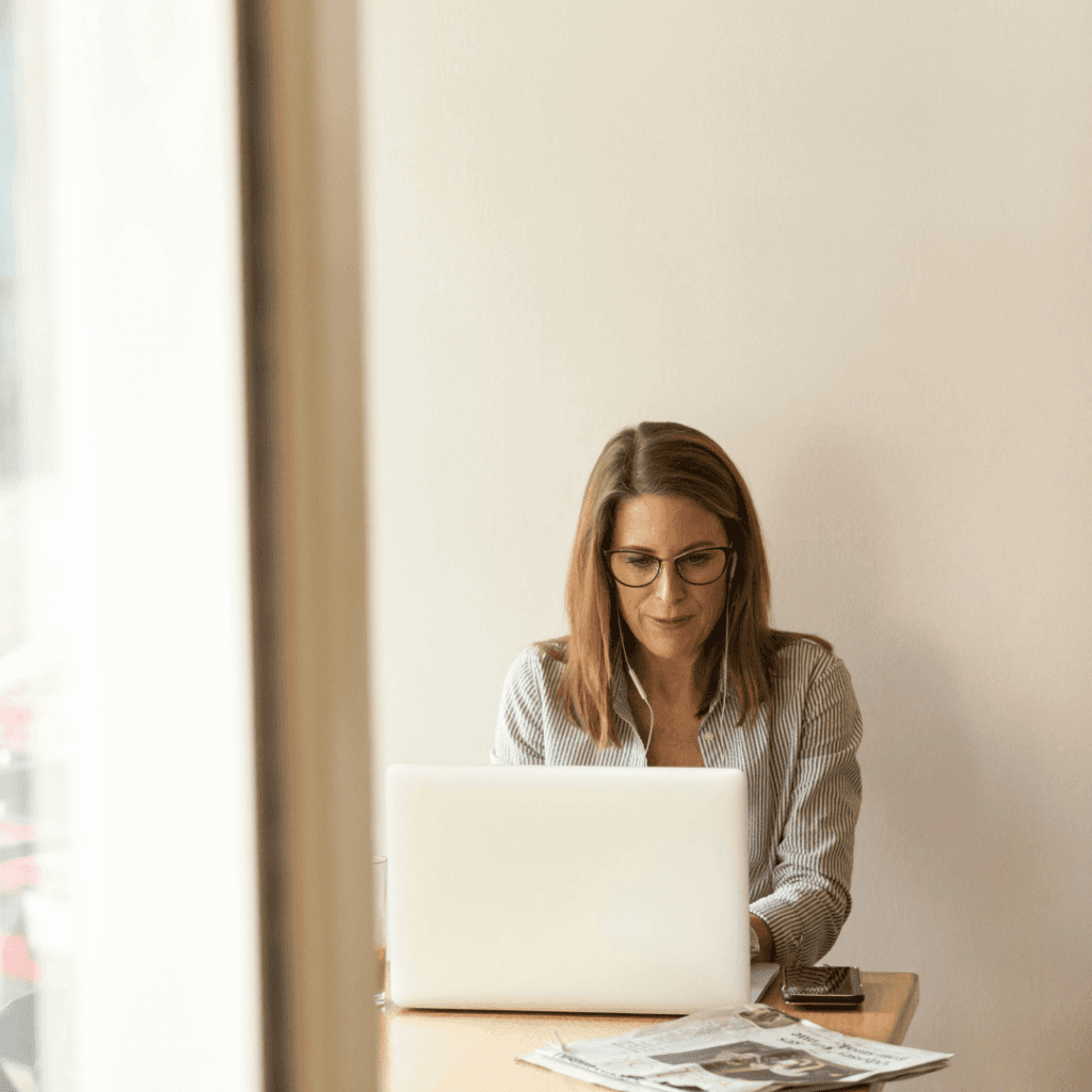 A focused woman analyzing a Website Optimization Report on her laptop in a well-lit workspace, representing the diligence needed for website analysis and optimization.