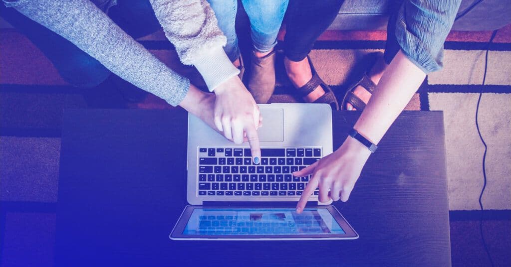 Two people pointing at a laptop screen, representing teamwork and Google Looker Studio data collaboration.