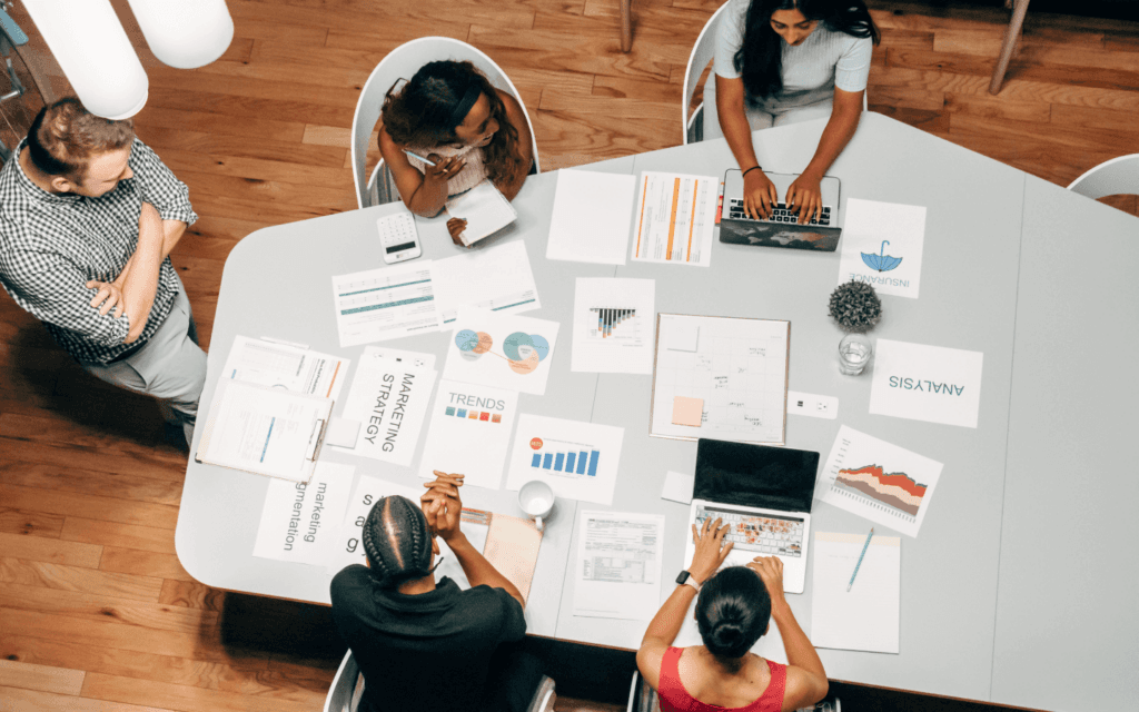 Business team collaboratively analyzing marketing and SEO strategies with documents and a laptop, indicative of using the Best SEO Report Software for data analysis.