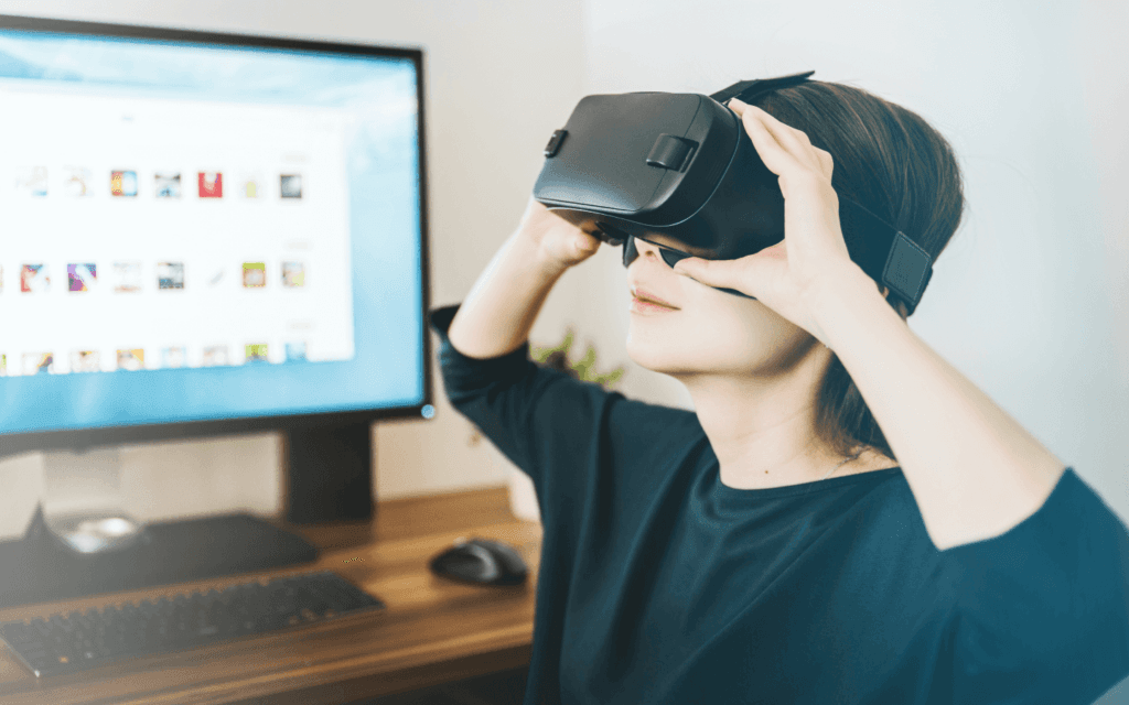 Person using a virtual reality headset to experience the latest digital marketing innovations, with a computer screen in the background.