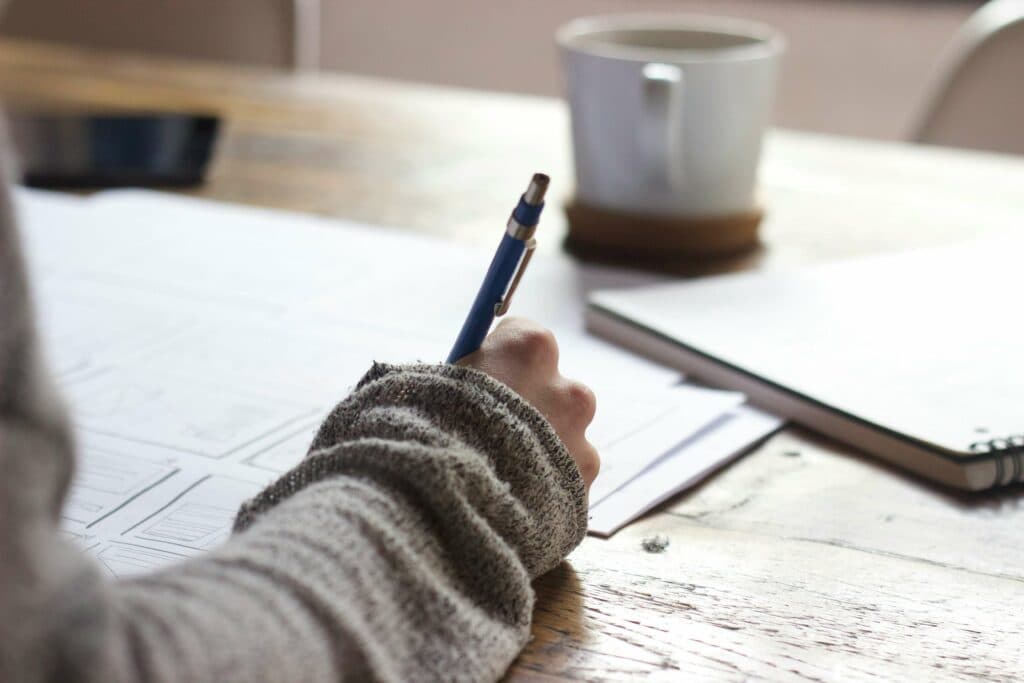 Person writing notes on paper with a cup of coffee, representing the use of free AI tools for digital marketing agencies to enhance strategy planning.