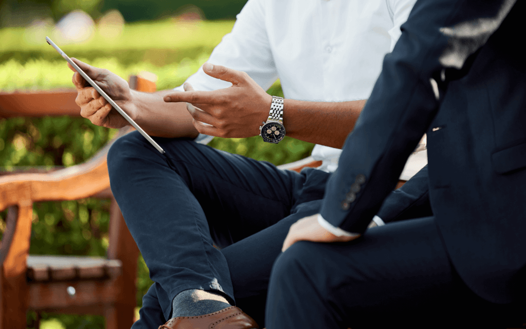 Two professionals in a park discussing data on a tablet using custom reporting tools, with one person pointing at the screen and the other holding the tablet.