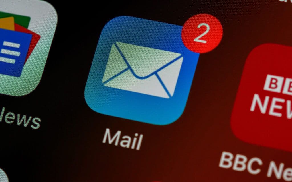 Smartphone screen zoomed in on an email app icon with a red notification for two unread messages, indicating the arrival of an Email Campaign Report, with other application icons in soft focus in the background.