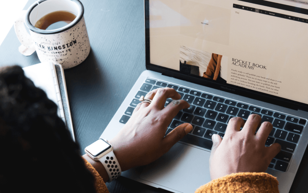 Overhead view of a digital marketer's hands typing on a laptop, with a coffee mug and a notebook, symbolizing the use of digital marketing innovations in content development."