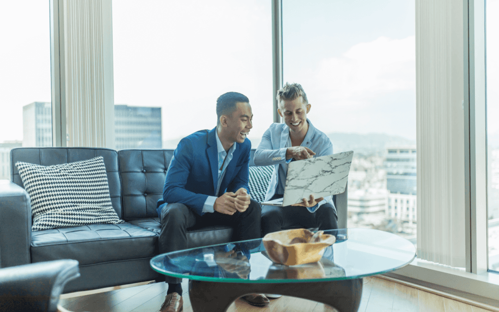 Two professionals engaged in a discussion over a laptop, possibly evaluating the Best SEO Report Software, in a bright office with expansive city views.