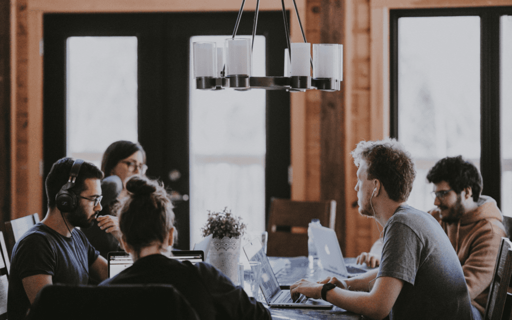 Marketing team engaged in discussion around a table with laptops, indicative of a strategic session utilizing marketing management tools to optimize their campaigns.