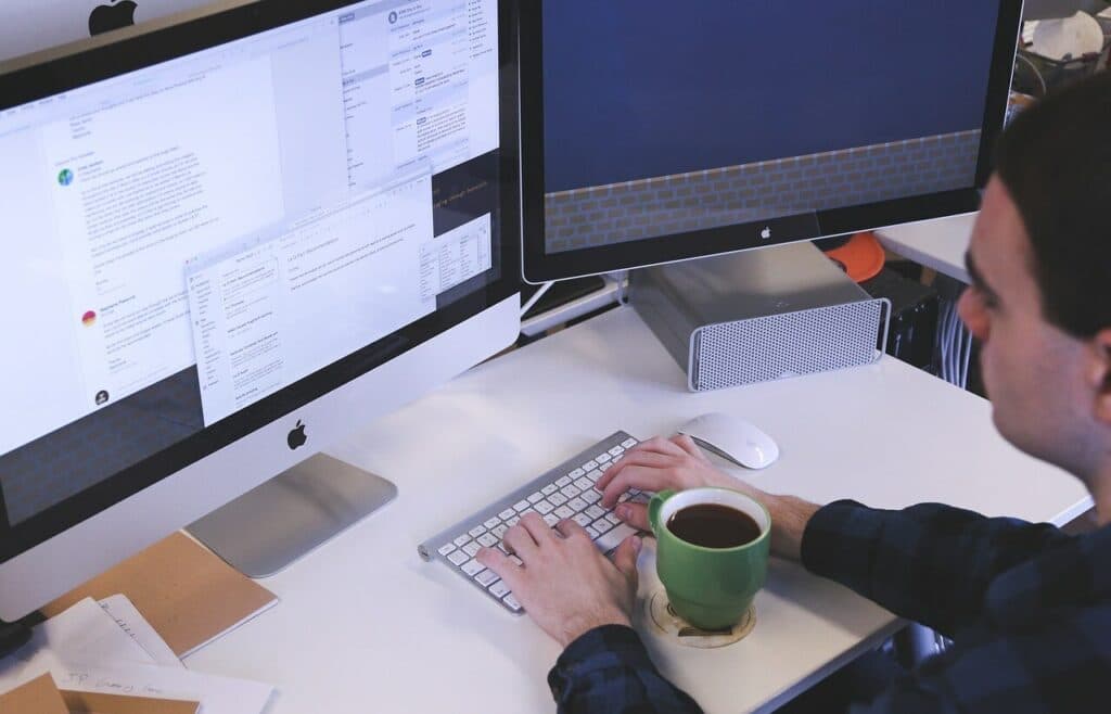 Person working on dual monitors with coffee, representing digital marketing agencies using free AI tools for productivity and task automation.