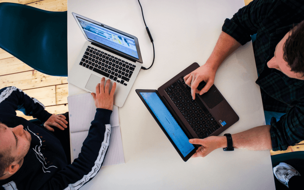 Two individuals collaborating over laptops with a focus on a Website Optimization Report, highlighting teamwork and the exchange of digital marketing strategies.