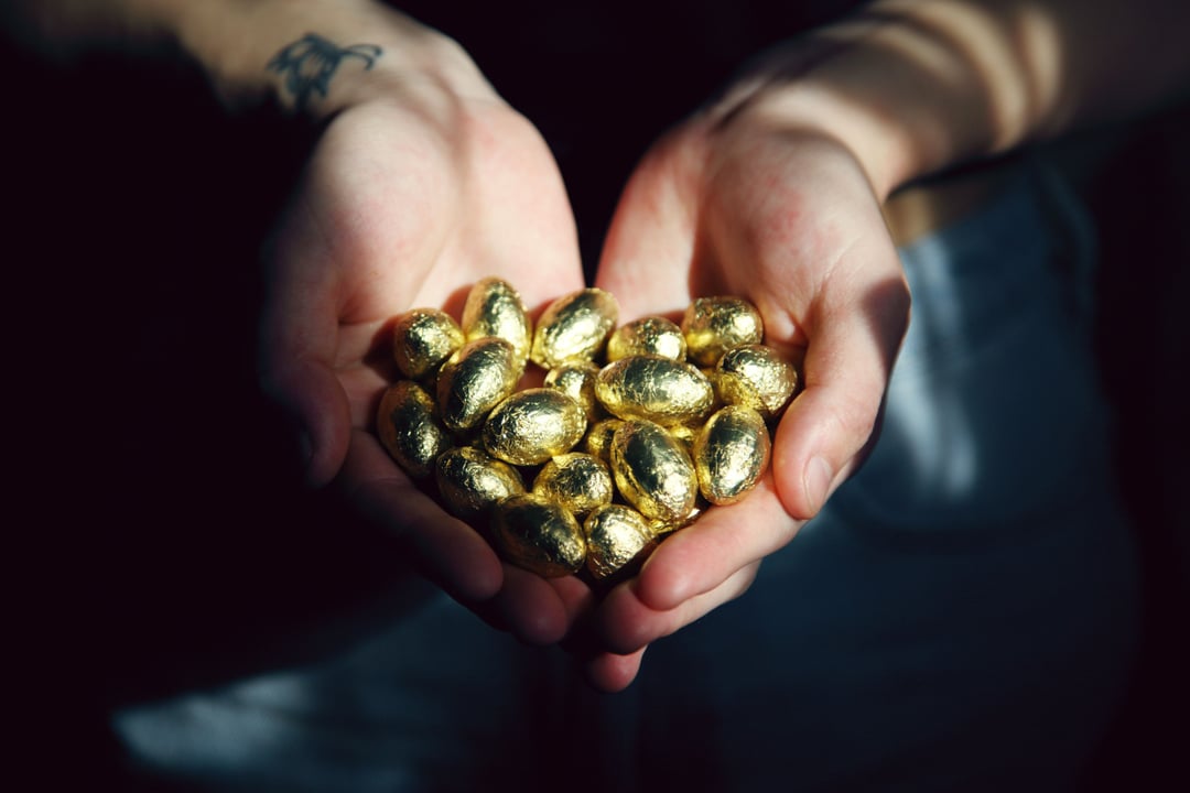 An image of two hands holding golden chocolate eggs.