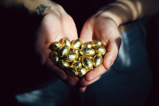 An image of two hands holding golden chocolate eggs.