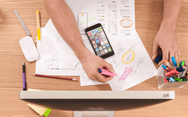 Hands highlighting key points on a document for a Keyword Research Report, with a smartphone and office supplies on the desk.
