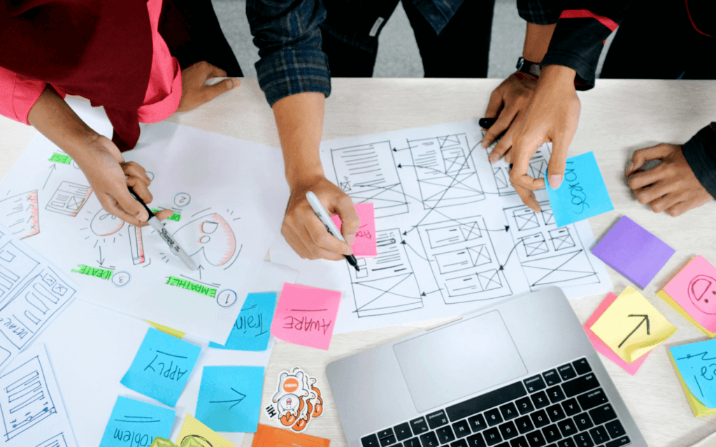 Overhead view of a team's hands engaged in wireframing and brainstorming with sticky notes, representing the creative stage of a Digital Agency Workflow.