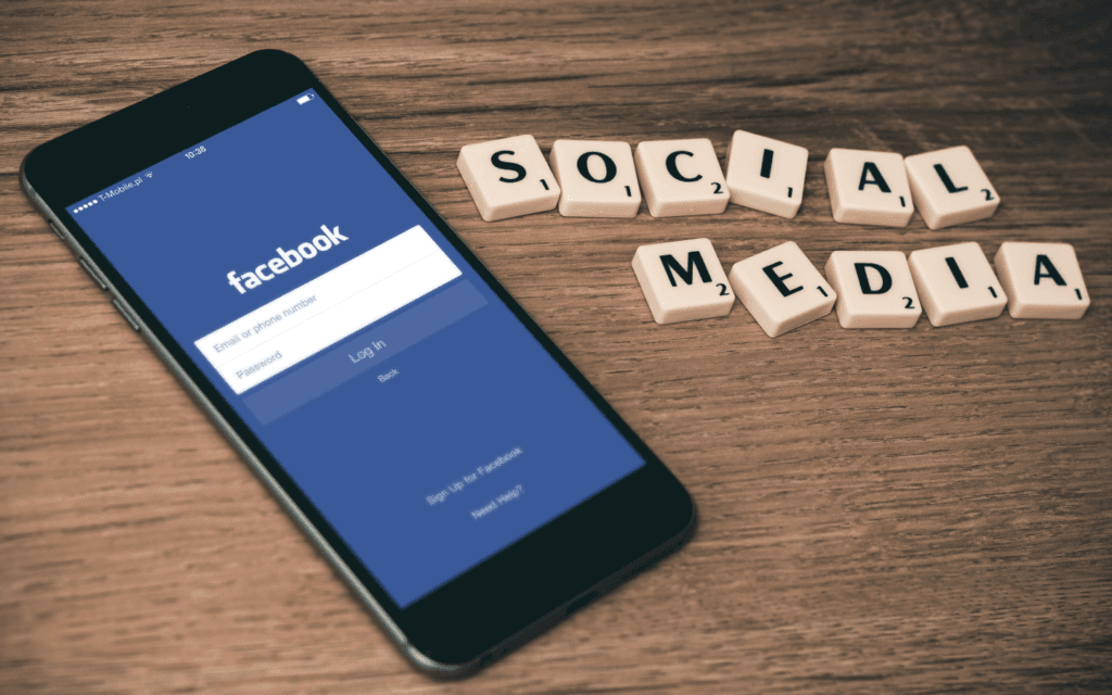 A smartphone displaying the Facebook login page rests on a wooden background, flanked by Scrabble tiles spelling "SOCIAL MEDIA," highlighting the integration of social platforms in content in social media marketing strategies.