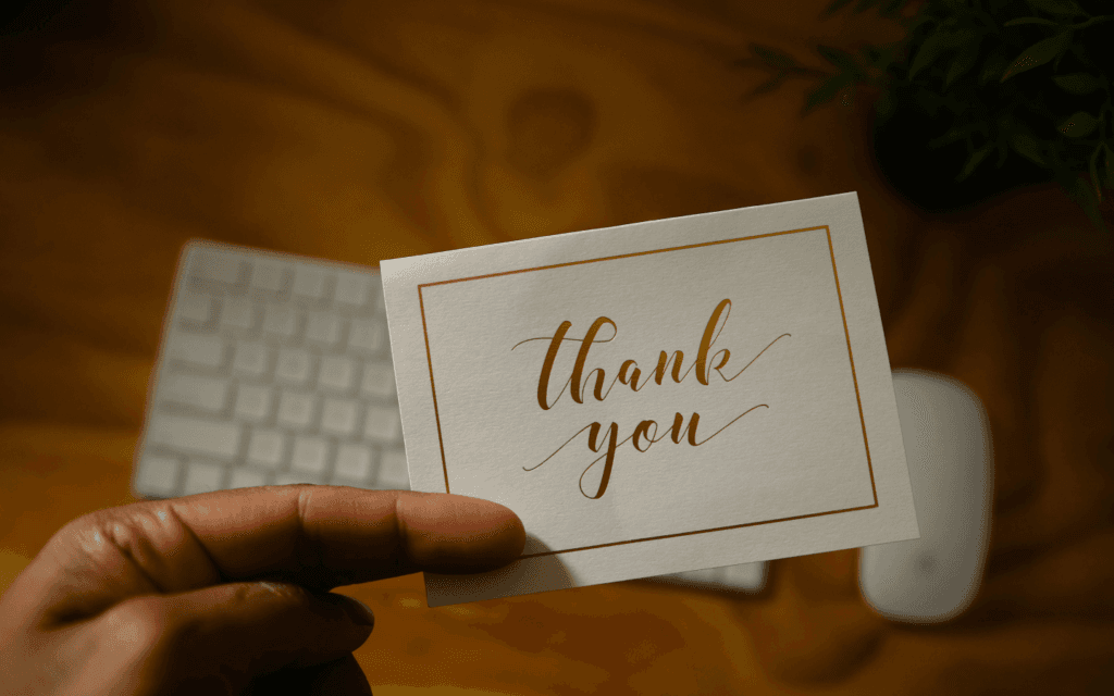 Hand holding a thank you card against a leafy backdrop, symbolizing appreciation in client retention efforts.