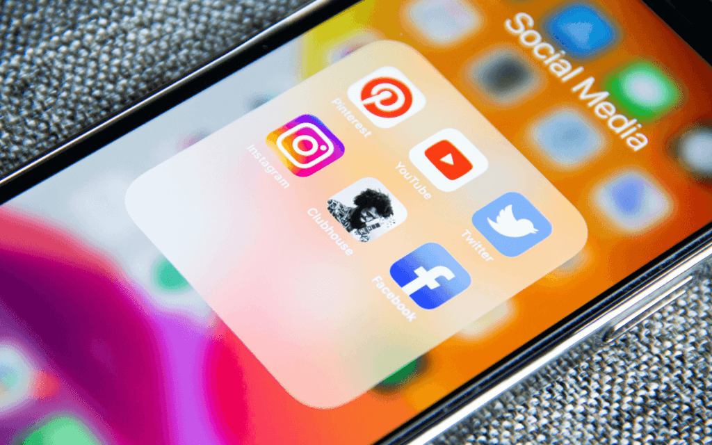 Smartphone screen with a 'Social Media' folder containing apps like Instagram, Pinterest, YouTube, Clubhouse, Twitter, and Facebook, integral for content distribution in social media marketing.
