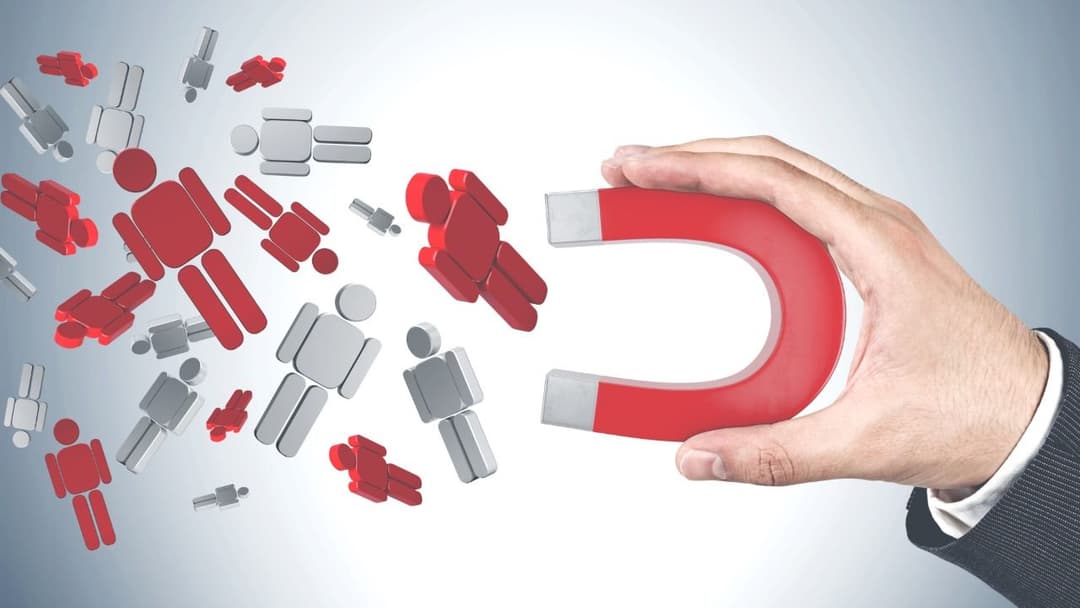Hand holding a red horseshoe magnet attracting figures symbolizing the effectiveness of lead magnets in drawing in potential leads for business growth.