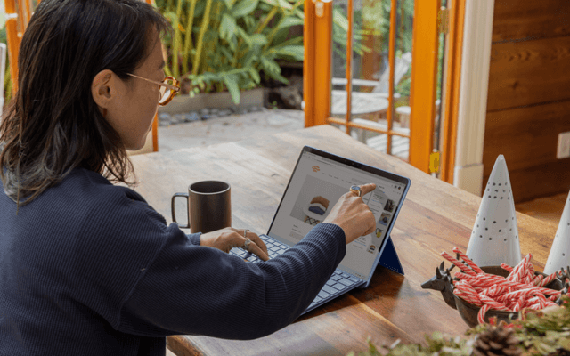 Person using a stylus on a tablet displaying custom reporting tools, seated at a wooden table with holiday decorations and a garden view in the background.