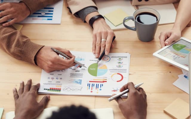 Two professionals analyzing a printed report with KPI charts and graphs, using digital KPI reporting tools to track performance metrics.