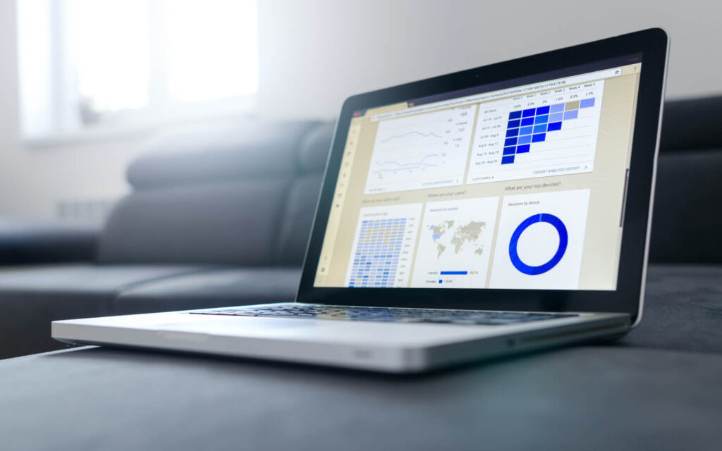 Laptop on a desk displaying dashboard and reporting software with detailed data visualizations including graphs and geographical user distribution.