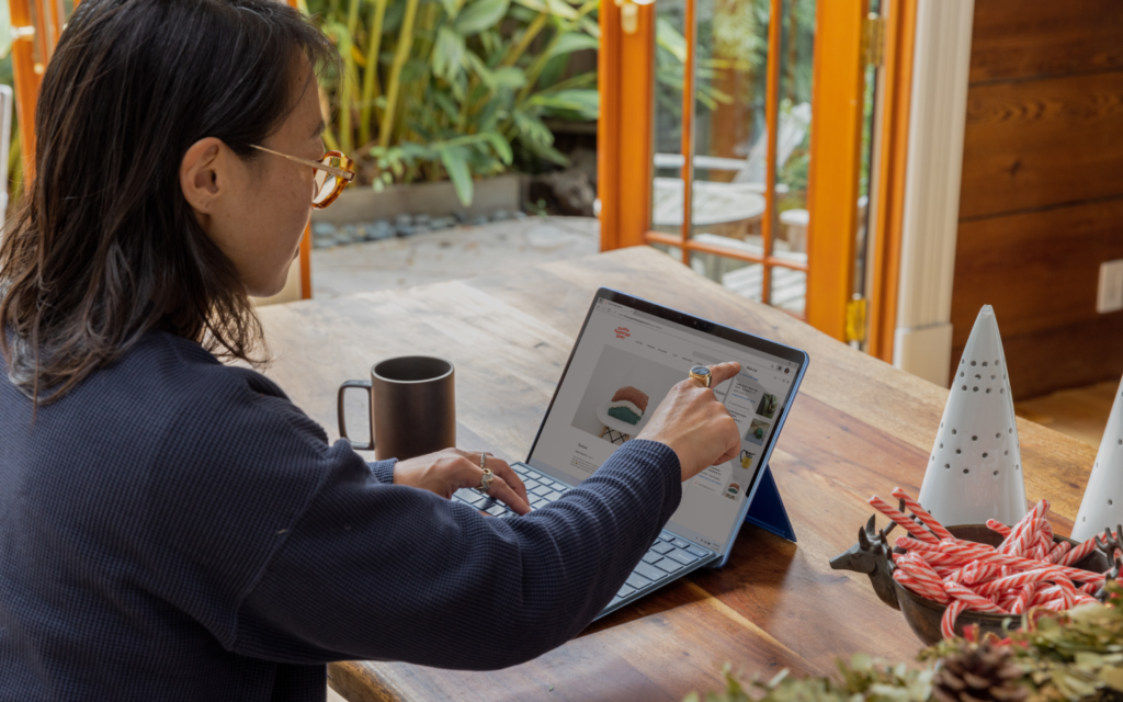 Efficient Business Analysis With Custom Reporting Tools - A Blend Of Comfort And Technology Person using a stylus on a tablet displaying custom reporting tools, seated at a wooden table with holiday decorations and a garden view in the background.