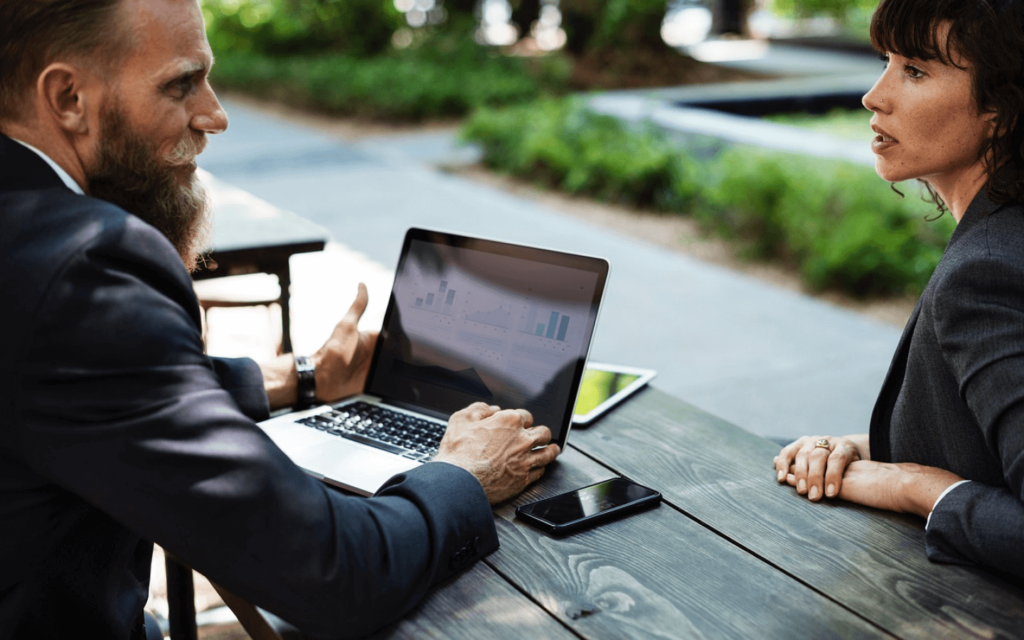 Business meeting with a focus on search engine marketing reporting software, showing a bearded man presenting analytics on a laptop to a female colleague.