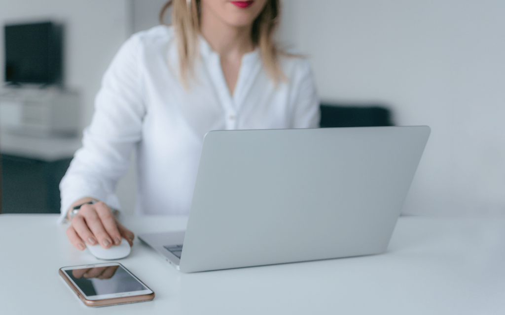 A professional working on a laptop with a smartphone on the desk, possibly reviewing a PPC report template for digital marketing analytics.