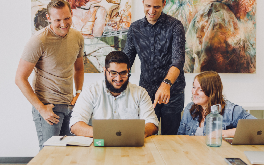 A team of marketers collaborating over a PPC report template on their laptops, with expressions of engagement and teamwork in a well-lit office.