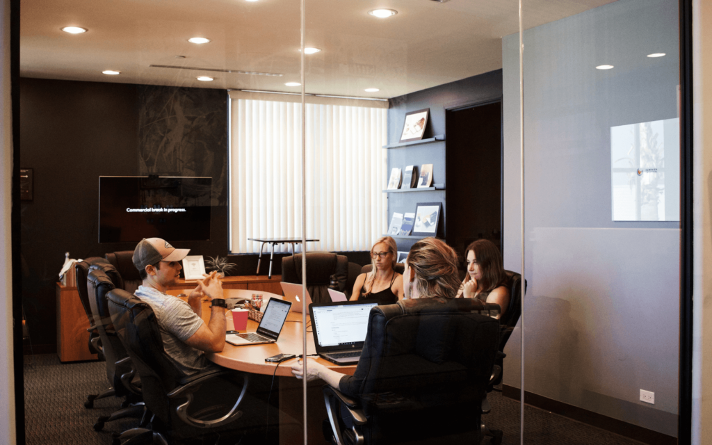 A team of professionals in a conference room, possibly strategizing over an All in One Digital Marketing Platform, with laptops and a paused screen in the background.