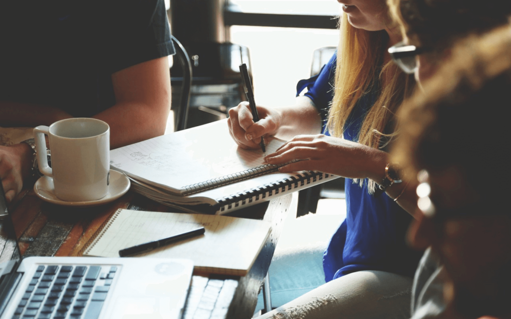 A team brainstorming over notebooks and a laptop, possibly strategizing for an All in One Digital Marketing Platform, in a setting that combines comfort with productivity.